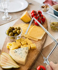 Six Inch Stainless Steel Cheese Slicer Handheld Wire Cutter cutting smooth slices of cheese on a wooden charcuterie board.