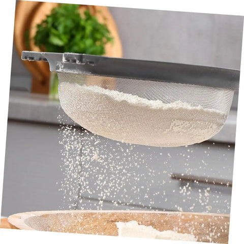 Flour being sifted through a mesh strainer in a kitchen setting.