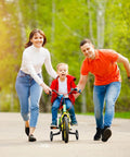 Child riding a bike with Quiet Training Wheels Kit for 12-20 inch kids bikes, guided by parents on a sunny day.