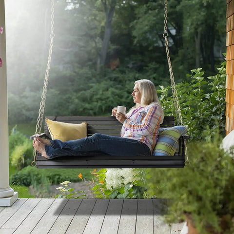 Woman relaxing on an upgraded patio wooden porch swing for courtyard and garden, heavy duty 880 lbs swing chair with black finish.