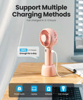 Mini Portable Handheld Fan With Base 3 Speed USB Rechargeable Dual Use Desk And Personal Fan Pink on wooden desk charging