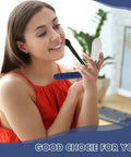 Woman holding a compact mirror in a modern workspace with a plant and desk in the background.