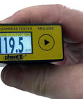 Hand holding Phase II SRG-2200 Mini Surface Roughness Tester Profilometer and Roughness Gauge displaying measurement on screen.