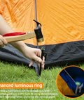 Person hammering Heavy Duty 8 Inch Tent Stakes Set With Metal Pegs Fluorescent Silicone Rings And Storage Bag For Camping into grass