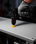 Close-up of cordless drill with yellow hole saw bit cutting into a metal panel.