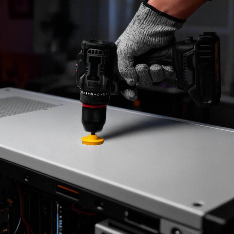 Close-up of cordless drill with yellow hole saw bit cutting into a metal panel.