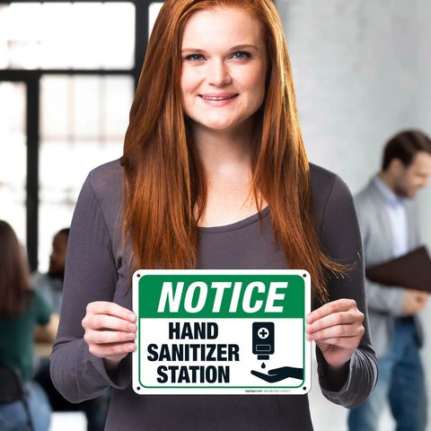 Wall Mounted Hand Sanitizer Station Sign For Offices Lobbies Or Schools Lightweight Polystyrene Frame Quick Peel Stick Mount No Hassle Setup Legit Sturdy Indoor Display held by a person indoors.