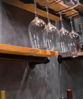 Vintage Industrial Iron Pipe Wine Rack For Badass Bar Setups And Dope Heavy Duty Countertop Organizer Wall Mounted Glass Bottle Holder displaying wine glasses on wooden shelves.