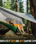 Person relaxing in a green Cozy Two Person Camping Hammock With Bug Net And Rain Fly Lightweight Double Parachute Nylon in the forest.
