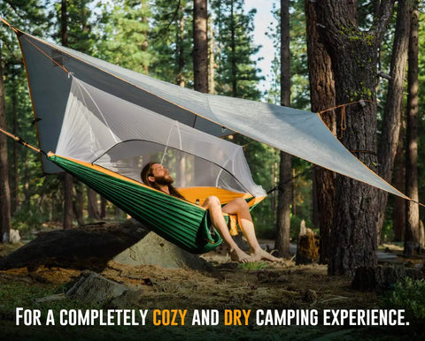 Person relaxing in a green Cozy Two Person Camping Hammock With Bug Net And Rain Fly Lightweight Double Parachute Nylon in the forest.