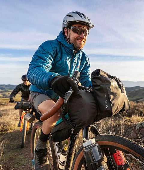 Cyclist with FrontLoader Bike Front Bag 8L for Light Camping Gear and Spare Clothes, green durable water-resistant build on mountain trail.