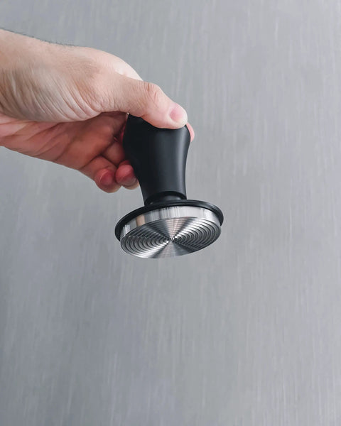 Hand holding Spring Loaded Espresso Tamper 53.3mm with ripple base and anodized aluminum handle, side view.
