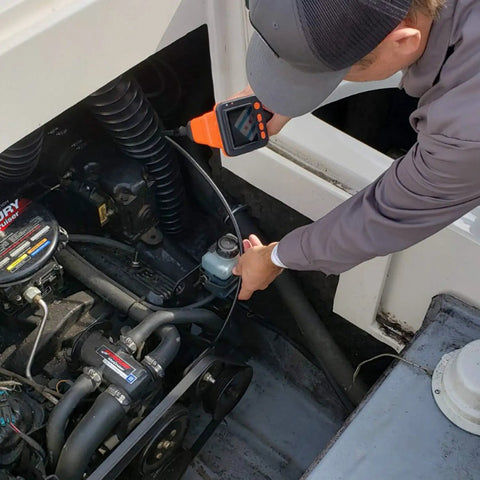 Mechanic using Camera Assisted Retrieval Tool With 32 Inch Bendable Gooseneck Four Prong Claw Live 480P Video On Two Point Eight Inch LCD Four LED Lights Magnetic Tip Pulls Ferrous Objects From Tight Spaces For Contractors Mechanics And DIY Pros Orange to inspect engine area.
