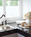 Oakmont Two Handle Kitchen Faucet With Side Sprayer In Oil Rubbed Bronze, Victorian style on kitchen sink near window.