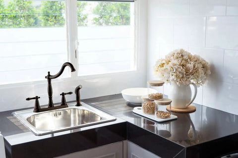 Oakmont Two Handle Kitchen Faucet With Side Sprayer In Oil Rubbed Bronze, Victorian style on kitchen sink near window.