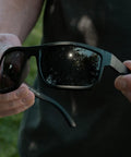 Kickass Z87 Certified Wayfarer Safety Sunglasses Featuring Hella Effective Antifog Smoke Lenses And Totally Shatterproof Matte Black Frames Built Tough For Male Workers held in hands outdoors