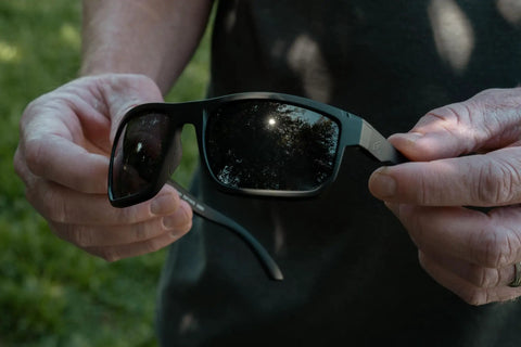 Kickass Z87 Certified Wayfarer Safety Sunglasses Featuring Hella Effective Antifog Smoke Lenses And Totally Shatterproof Matte Black Frames Built Tough For Male Workers held in hands outdoors