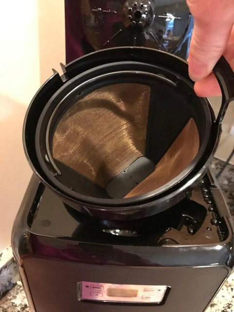 Hand holding Gold Tone Permanent Coffee Filter for 12 cup coffee makers including Krups Savoy Braun DeLonghi, placed in machine