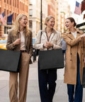 Three women carrying 400 Pack Black Paper Gift Bags 16x6x12 Inches With Handles Made From Recycled Kraft Paper in city street.