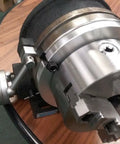 Close-up of 8 Inch Precision Horizontal Vertical Rotary Table With 6 Inch Three Jaw Chuck and adjustment lever on wooden table.