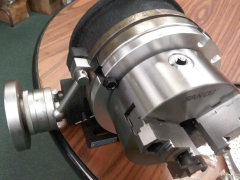 Close-up of 8 Inch Precision Horizontal Vertical Rotary Table With 6 Inch Three Jaw Chuck and adjustment lever on wooden table.