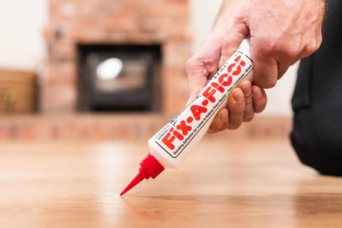 Hand applying All In One Floor Repair Adhesive For Loose Hollow Tiles And Creaky Wood From A Simple Squeeze Tube With Precision Tip