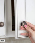 Hand installing oil rubbed bronze cabinet knobs one and one quarter inch round drawer handles on white kitchen cabinet door
