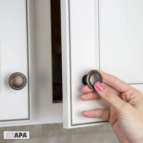 Hand installing oil rubbed bronze cabinet knobs one and one quarter inch round drawer handles on white kitchen cabinet door