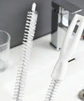 Flexible Drain Snake Cleaner Brush That Kicks Out Greasy Gunk Reusable Spiral Hair Removal Tool With Comfort Grip Handles For Sinks Showers And Bathtubs In White on a bathroom sink.