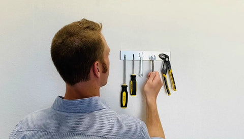 Man hanging tools on a wall using Magnetic Paint And Primer For Any Surface High Yield Black 8 Oz Turns Walls Into A Magnetic Canvas.