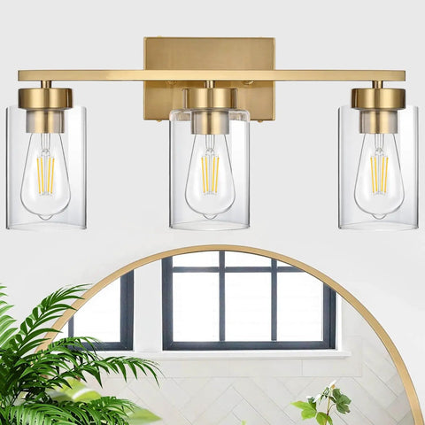 Clean Three Light Bathroom Vanity Wall Sconce In Smooth Brushed Gold Finish With Clear Retro Glass Shades, viewed from front with mirror.
