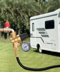 Solid Brass RV Water Pressure Regulator With Built In Gauge And Adjustable Valve connected to an RV in a grassy area.