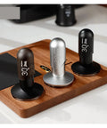 No Drama 2 In 1 Coffee Tamper And Constant Pressure Espresso Distribution Tool With Calibrated Spring For Even Powder Pressing And Flawless Puck Prep In 58mm Silver on a wooden tray with black and silver variations.