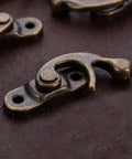 Close-up of Vintage Swing Arm Latch Set in Antique Brass with Decorative Horn Lock on leather surface