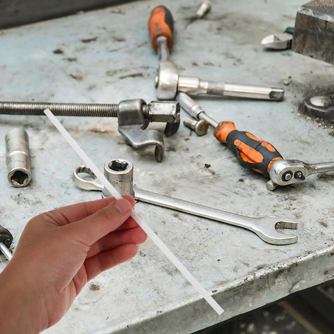 Person holding a 20cm white PP plastic welding rod among various tools on a garage workbench for car repairs.