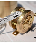 Top Shelf Vintage Brass Mini Tape Measure With Retractable Sewing Ruler That Is Totally Built Tough For All Tailor Jobs Featuring One Meter Gauges. Close-up of brass measuring reel with 100 cm tape.