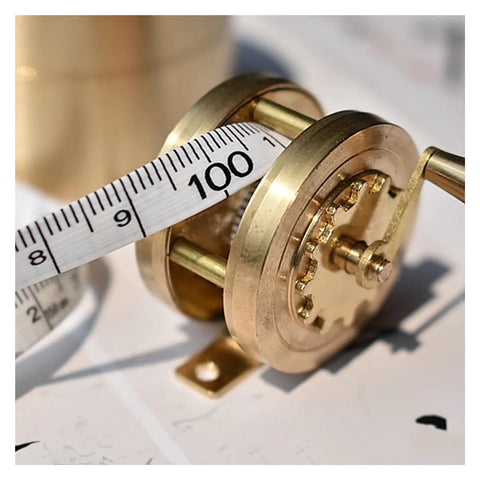 Top Shelf Vintage Brass Mini Tape Measure With Retractable Sewing Ruler That Is Totally Built Tough For All Tailor Jobs Featuring One Meter Gauges. Close-up of brass measuring reel with 100 cm tape.