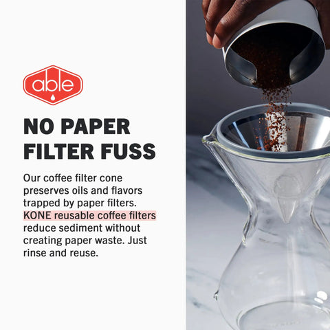 Hand pouring coffee grounds into Chemex with reusable stainless steel filter, no paper filter fuss text