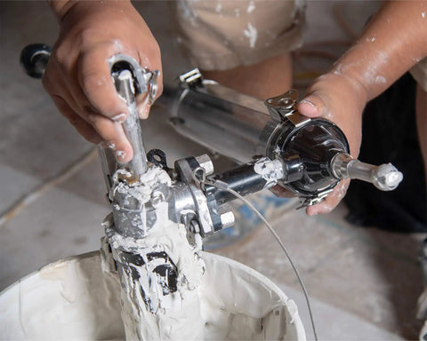 Close-up of hands using Drywall Box Filler Valve For Joint Compound Pumps, Heavy Duty Billet Aluminum Body With Hard Coat Anodized Finish.