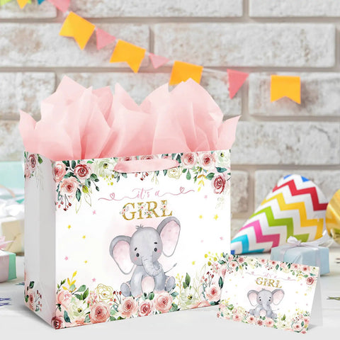 13 Inch Large Baby Shower Gift Bag For Girls With Pink Floral Elephant Design And Durable Handles Includes Tissue Paper Pack And Greeting Card No Fuss Quick Gift Wrapping For Baby Showers Or Birthday Parties displayed with pink tissue paper and greeting card on a decorated table.
