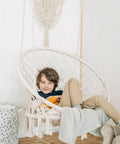 Child sitting in Bohemian Macrame Hammock Chair Swing With Hardware Kits For Indoor And Outdoor Use Ideal For Balcony Porch Yard Or Bedroom Cozy Supportive Knitted Seat With 265 Pound Capacity And Easy Hanging, indoors.