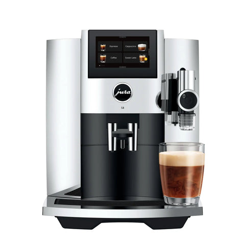 Premium Fully Automatic Chrome Espresso Coffee Machine Featuring A Hella Smooth Four Point Three Inch Smart Touchscreen Display For Twenty Seven Freshly Ground Drinks, black and chrome with a glass of espresso.