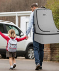Man carrying Gate Check Car Seat Travel Bag With Padded Interior For Air Travel Rugged Car Seat Carrier Backpack Fits Most Brands 17 X 17 X 28 Inches Grey Essential Baby Travel Gear while holding child's hand.