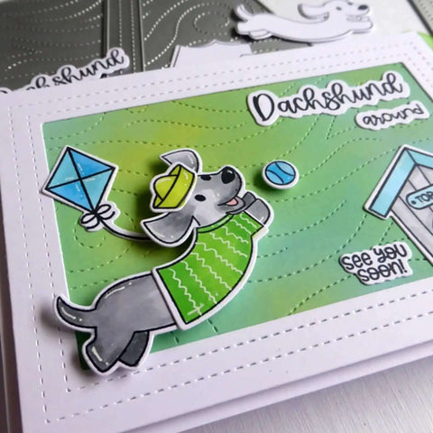 Handmade card featuring stitched rectangle frame die cuts, decorated with a dachshund illustration, kite, and playful sentiment on green background.