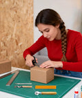 Woman using scissors on cardboard box with Top Tier 5 Piece Box Resizer Kit Featuring Scoring Wheel Perforator and tools on table.