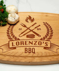 Front view of a wooden cutting board engraved with Lorenzo's BBQ logo, crossed tools; tomatoes and lime on the side.