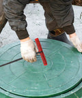 Heavy Duty Steel Manhole Cover Opener With Solid T Handle Grip Rust Resistant Multi Purpose Pull Lifter Hook For Sewer Lid Snagging And Jobsite Hauls No Sweat Tradesman Gear in use on green manhole cover.