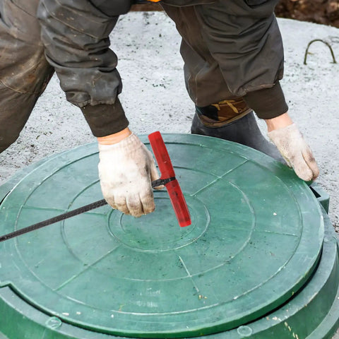 Heavy Duty Steel Manhole Cover Opener With Solid T Handle Grip Rust Resistant Multi Purpose Pull Lifter Hook For Sewer Lid Snagging And Jobsite Hauls No Sweat Tradesman Gear in use on green manhole cover.
