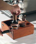 Person using Eight In One Espresso Knock Box And Barista Grade Coffee Accessories Organizer with Natural Walnut Base on counter.