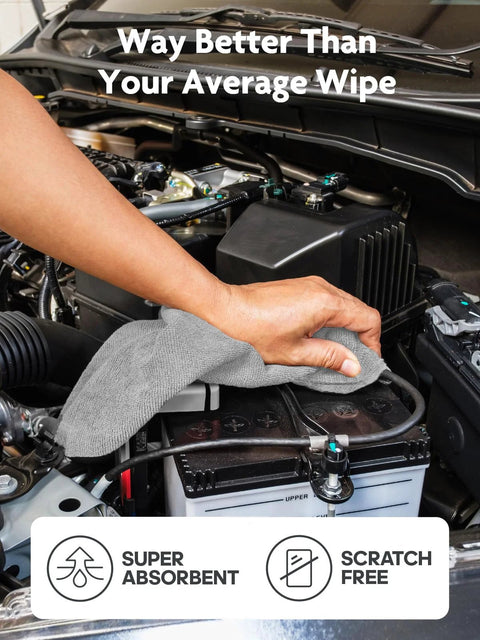 Gray microfiber cleaning cloth used to wipe a car battery in an engine bay.